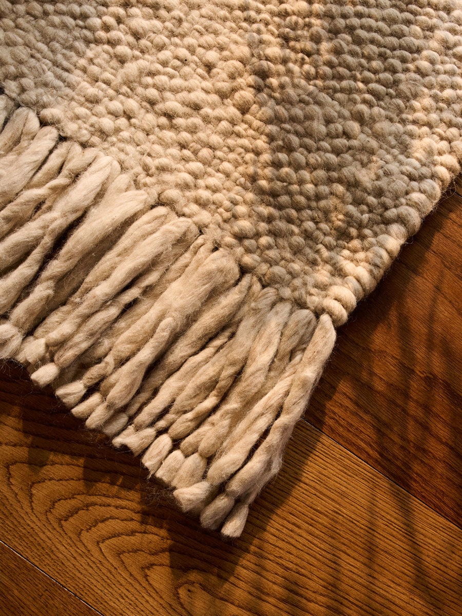 White wool rug with large fringes on a dark wooden floor