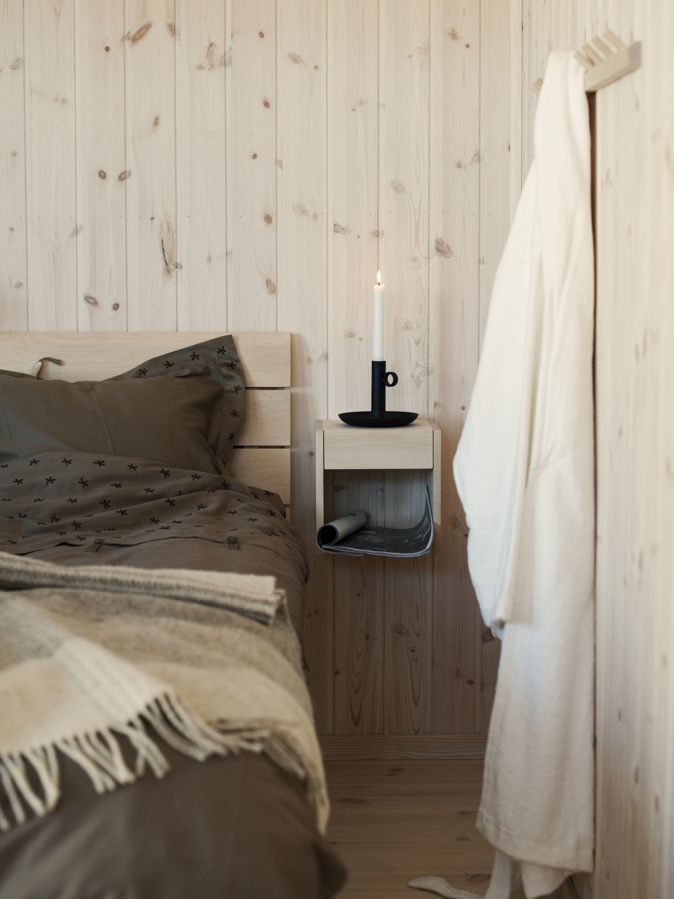made-up bed and bedside table in birch